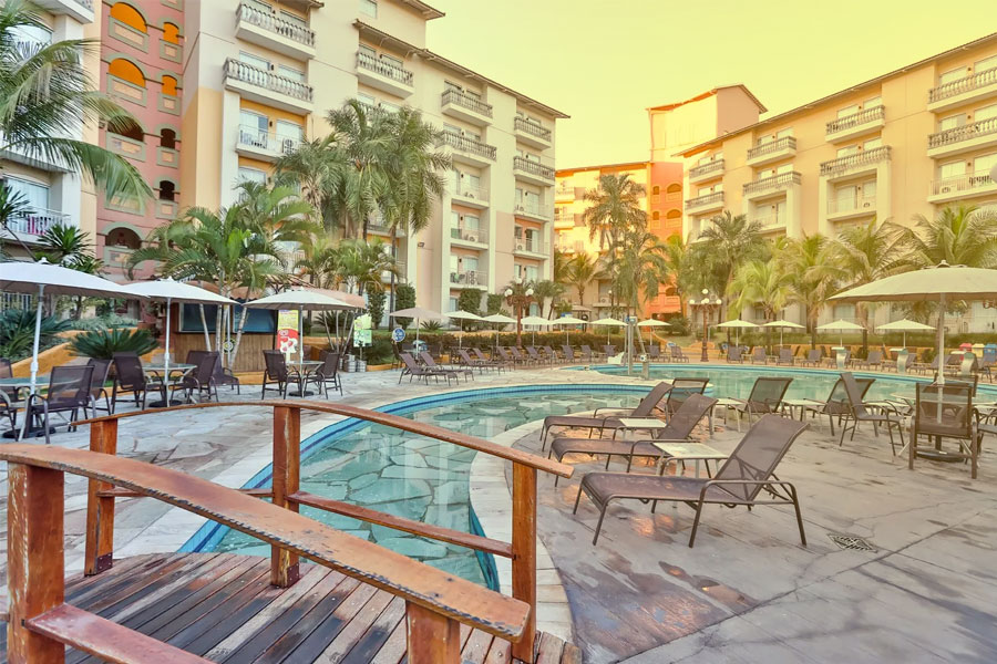 Cadeiras espreguiçadeiras, guarda-sóis e palmeiras ao redor da piscina do Nobile Resort Hotel. 
